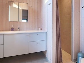 A modern bathroom with a wooden vanity, a mirror, and a shower area.