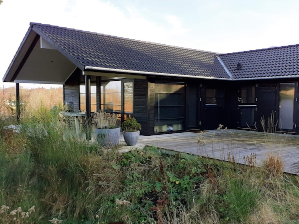A modern house with a sloped roof, large windows, and a covered patio area.