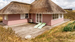 Ein rosafarbenes Holzhaus mit Strohdächern, einer Holzterrasse und einer grünen Rampe, die zum Eingang führt.