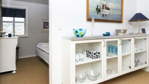 Ein Zimmer mit einem weißen Schrank, einem Bild eines Bootes, einer Lampe und einem Fenster mit Blick auf Bäume.