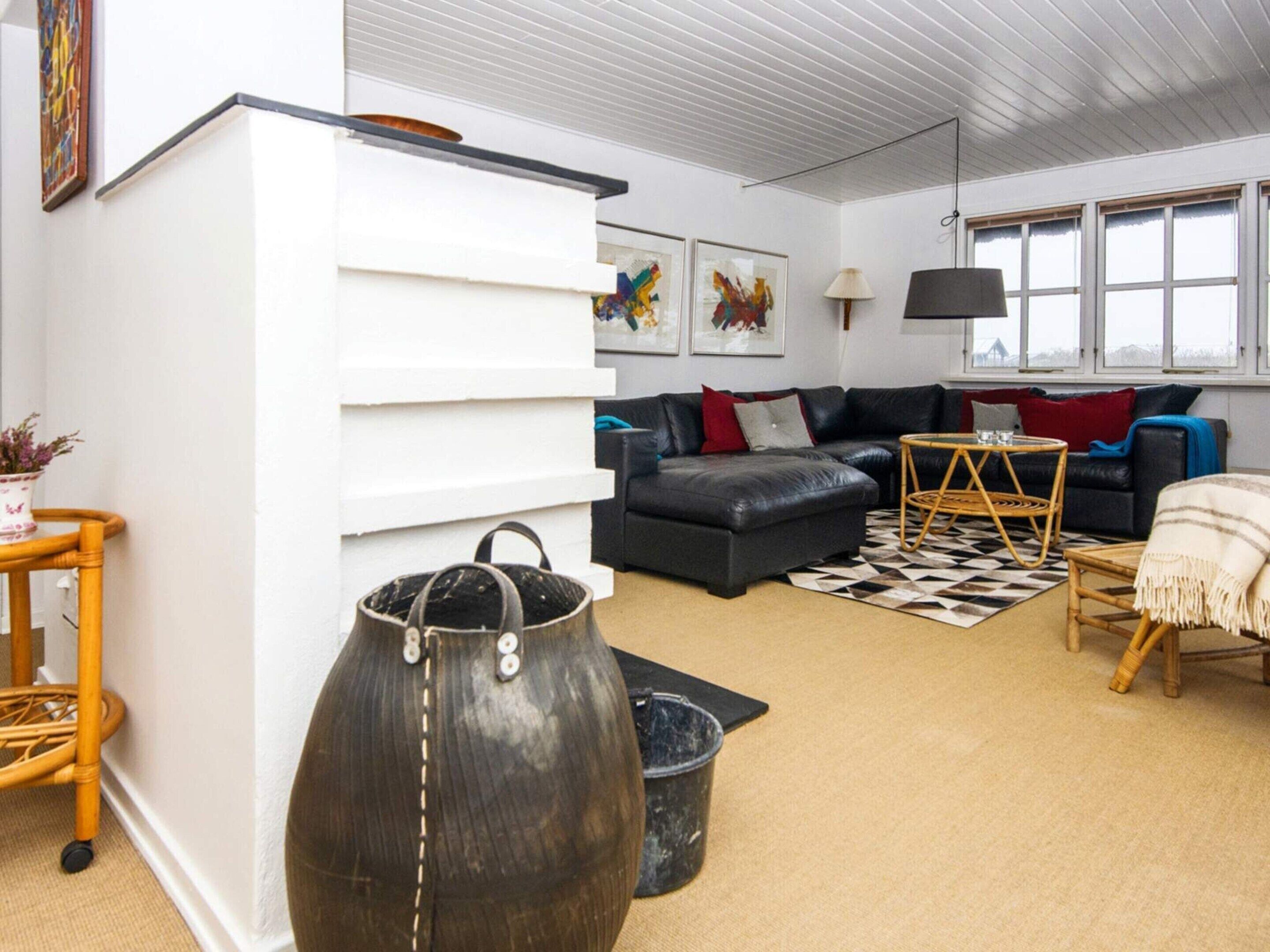 A modern living room with a black leather sofa, a white cabinet, and a large decorative vase.