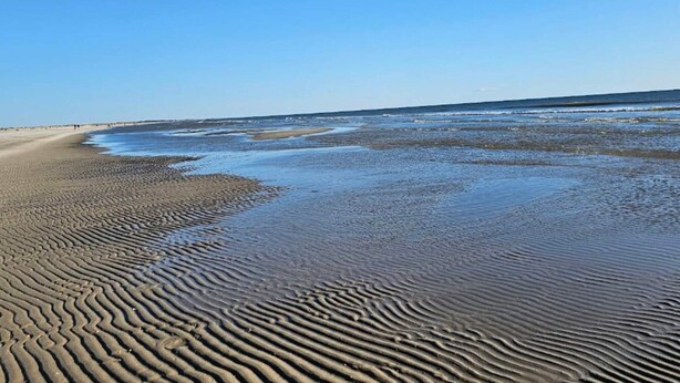 Ein Strand mit feuchten Sandmustern und einem klaren, blauen Himmel.
