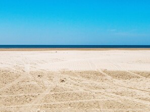 Ein weiter Sandstrand mit Spuren, die zum Wasser führen.