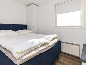 A bed with white bedding, a blue headboard, a window, and a white radiator. - 4 Star Holiday Home in Hjorring (Hjørring)