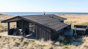 A beach house with a deck, outdoor seating, and a view of the ocean.