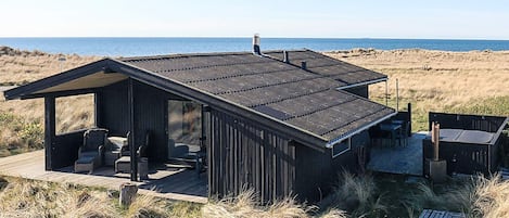 A beach house with a deck, outdoor seating, and a view of the ocean.