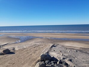 Une plage avec un ciel dégagé, un rivage sablonneux et quelques rochers éparpillés.