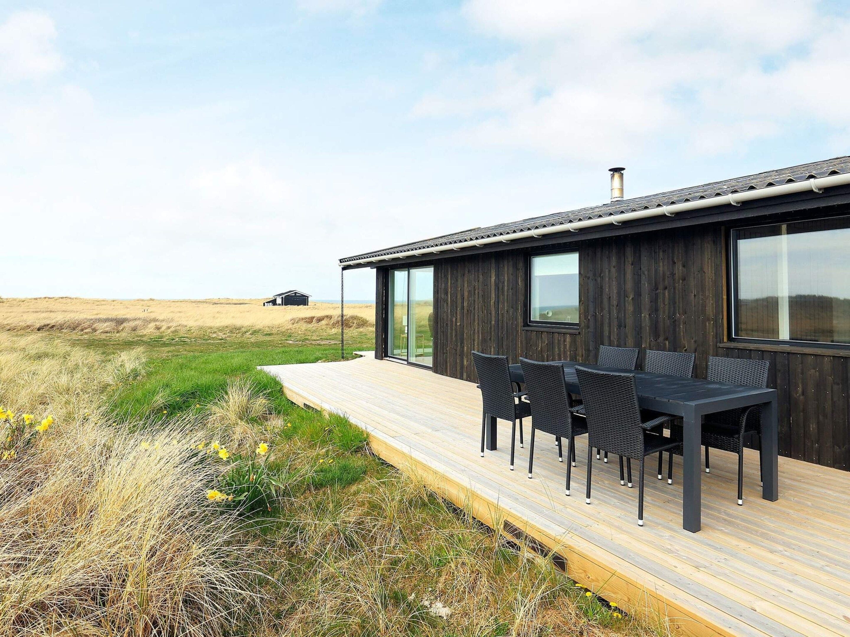 A modern house with a deck, outdoor seating, and a view of the landscape.