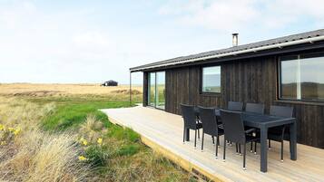 A modern house with a deck, outdoor seating, and a view of the landscape.