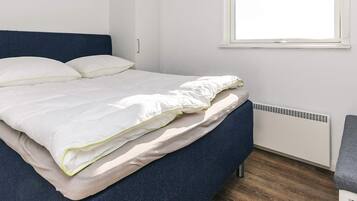 A bed with white bedding, a blue headboard, and a window with blinds.