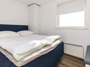 A bed with white bedding, a blue headboard, and a window with blinds.