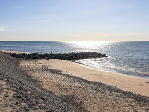 Une plage avec une digue rocheuse, un rivage sablonneux et une mer calme.