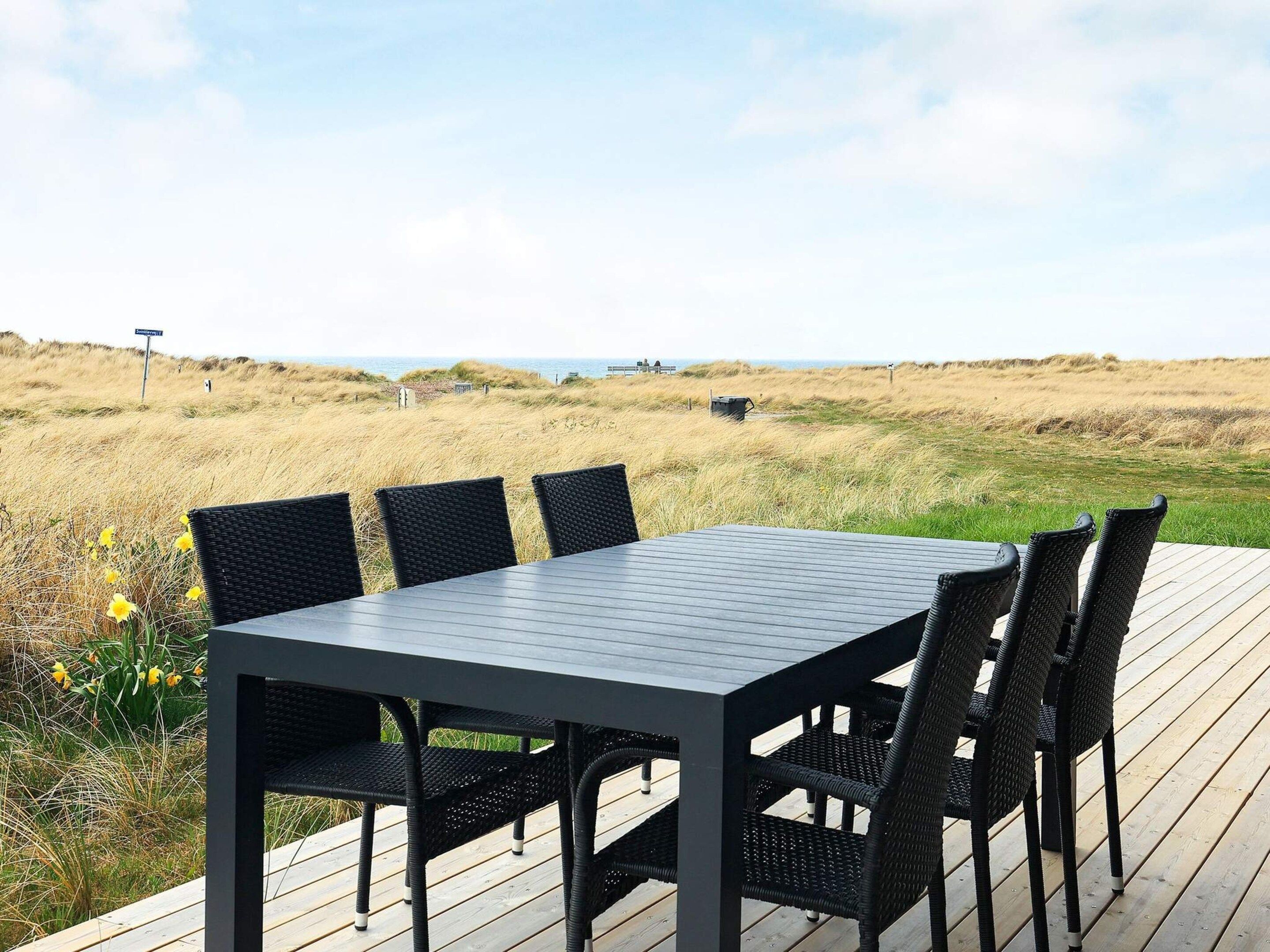 A deck with a table and chairs overlooking a beach.