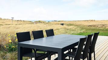 A deck with a table and chairs overlooking a beach.