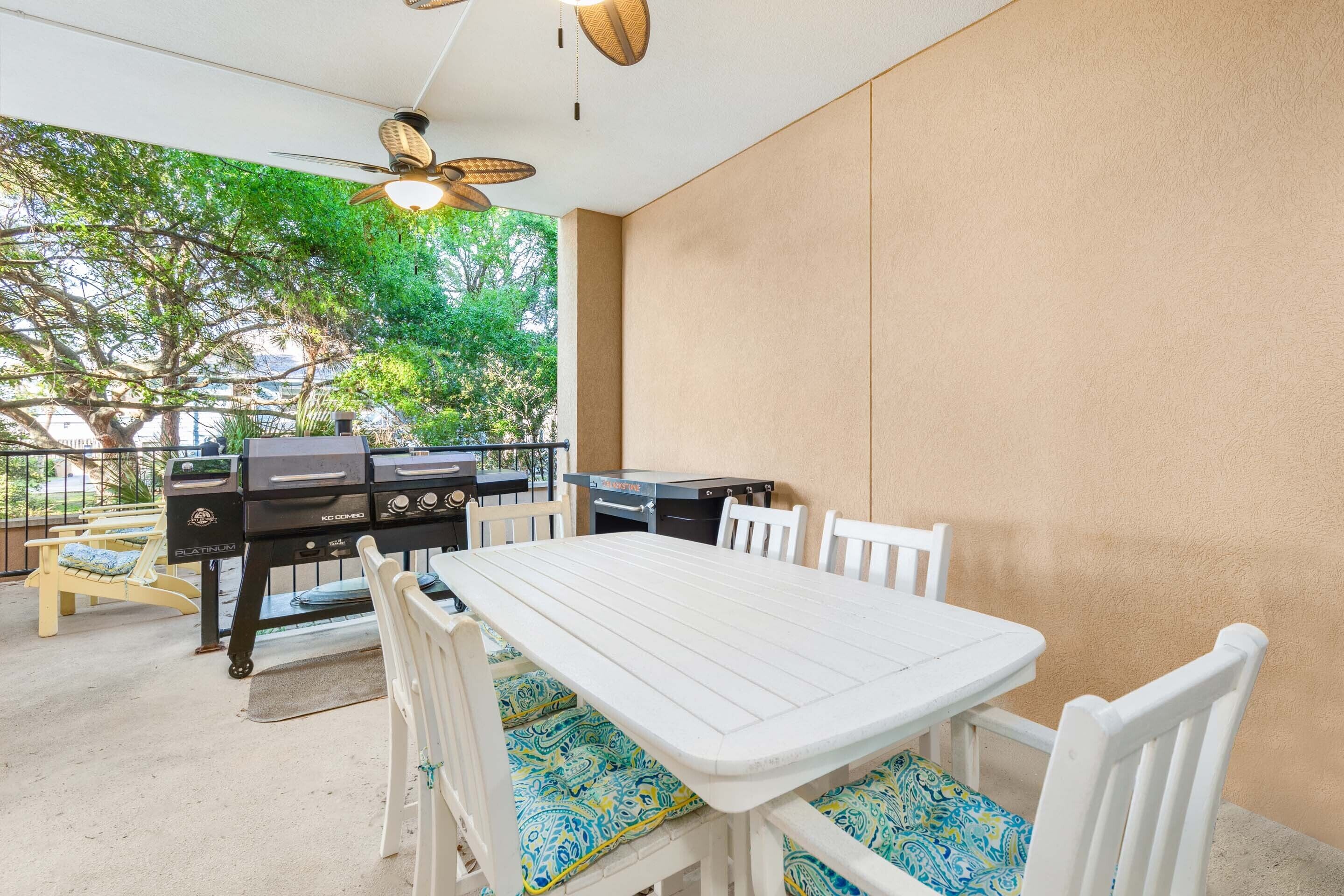 Eine Terrasse im Freien mit weißem Tisch und Stühlen, einem Grill und einem Deckenventilator.