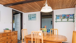 Un coin repas avec une table et des chaises en bois, un luminaire suspendu et une étagère murale contenant des livres.