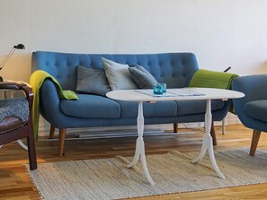 A blue sofa with a white table in front, a green throw blanket, and a striped rug on a wooden floor. - 6 Person Holiday Home in Bergkvara (Bergkvara)