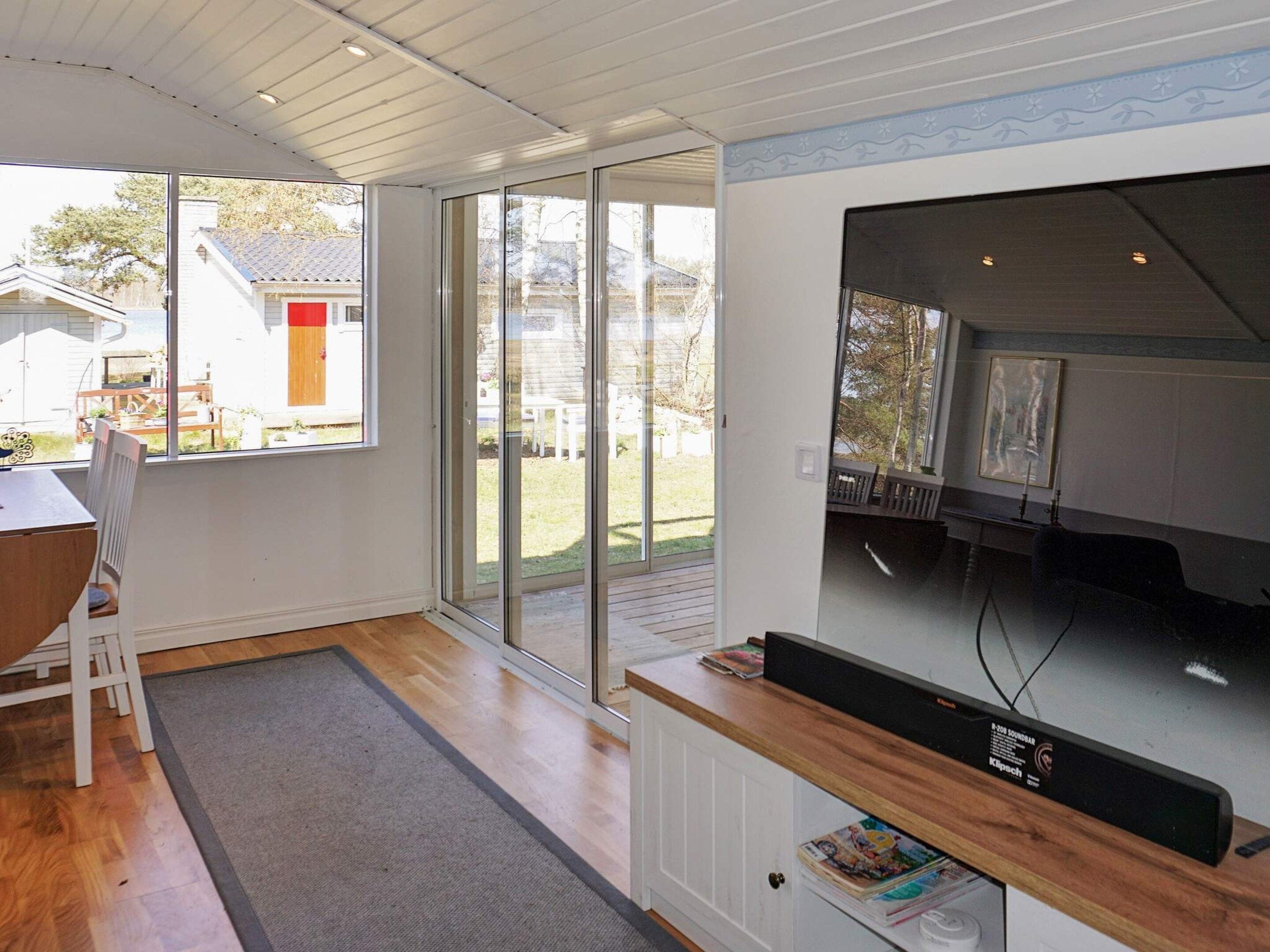 Una sala de estar moderna con un televisor de pantalla plana grande, puertas de vidrio corredizas que dan a un patio trasero y una mesa de comedor de madera con sillas.