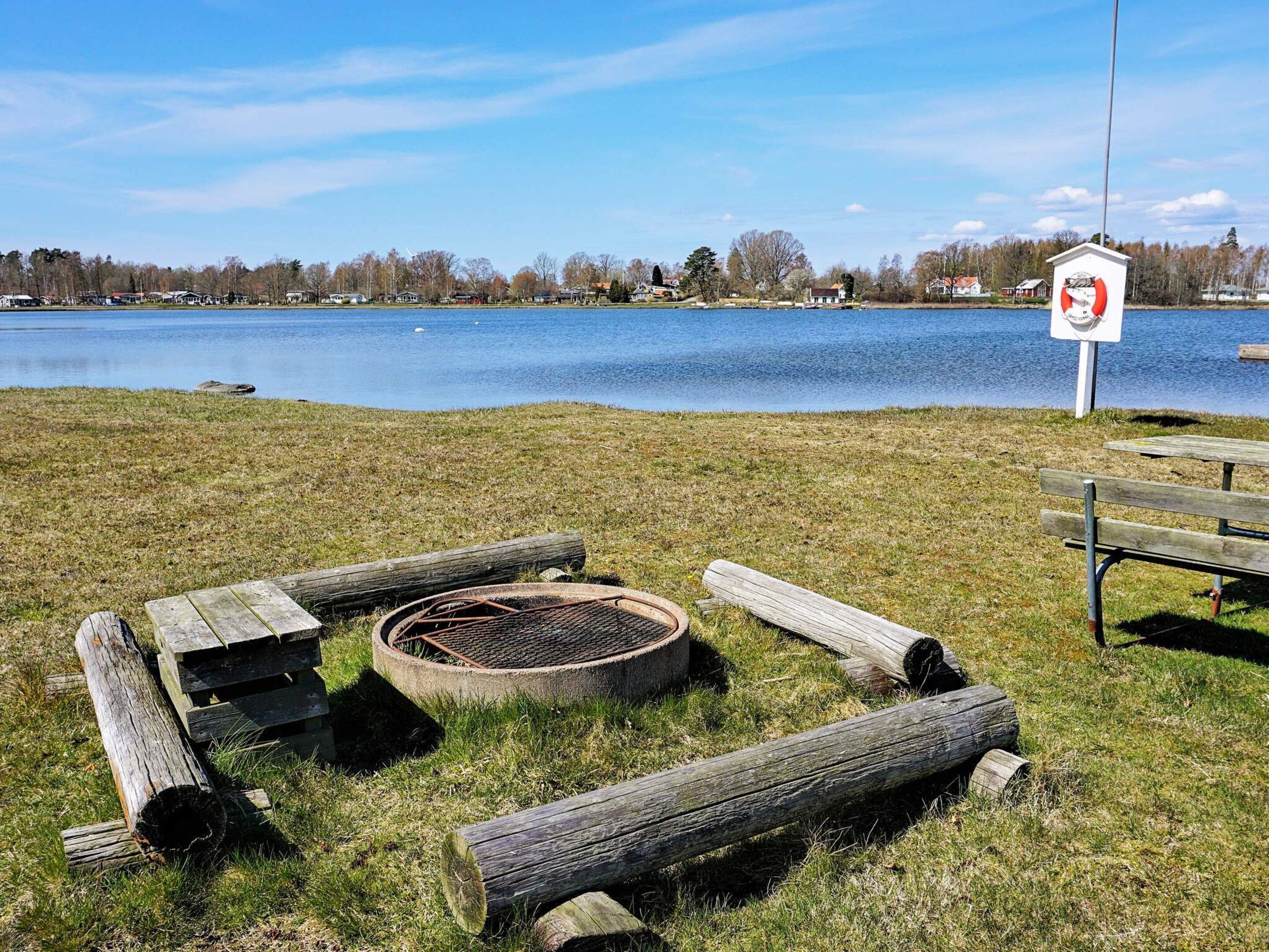 Un cadre idyllique au bord du lac, avec un foyer, des bûches et un banc.