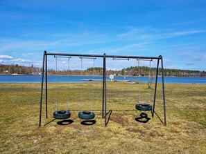 A swing set with tire swings in a grassy field with a lake and trees in the background.