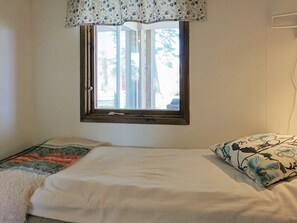 Ett sovrum med en enkel säng, ett fönster med en blommig gardin och en mönstrad kudde.
