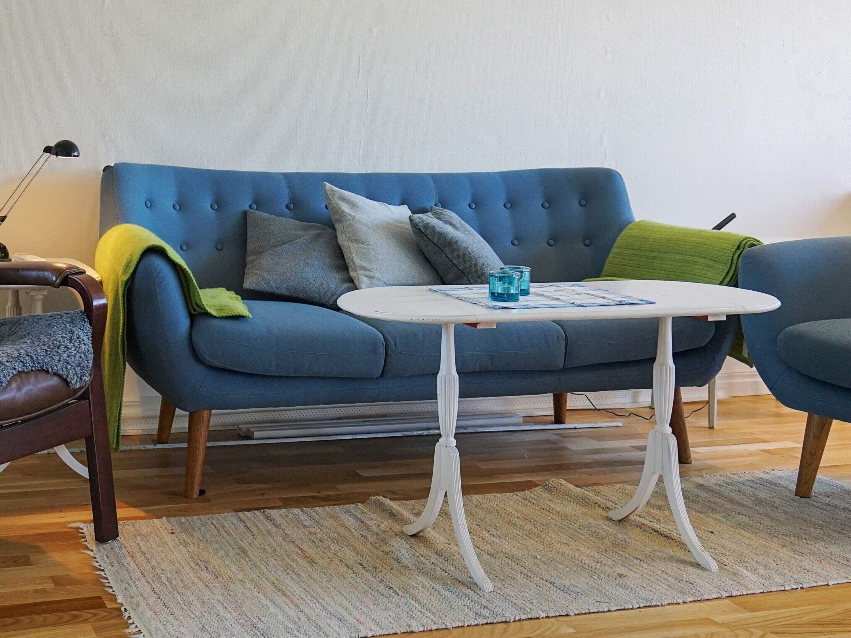 A blue sofa with a white table in front, a green throw blanket, and a striped rug on a wooden floor.