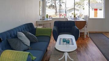 A room with a blue sofa, a white table with two glasses, and a view of a house through large windows.