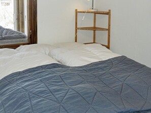 A neatly made bed with a quilted blanket, a bedside table with a lamp, and a window with a view of the outside.