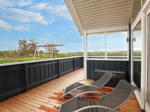 Une terrasse extérieure couverte, dotée d’un plancher en bois, d’une rambarde noire et offrant une vue sur le paysage.