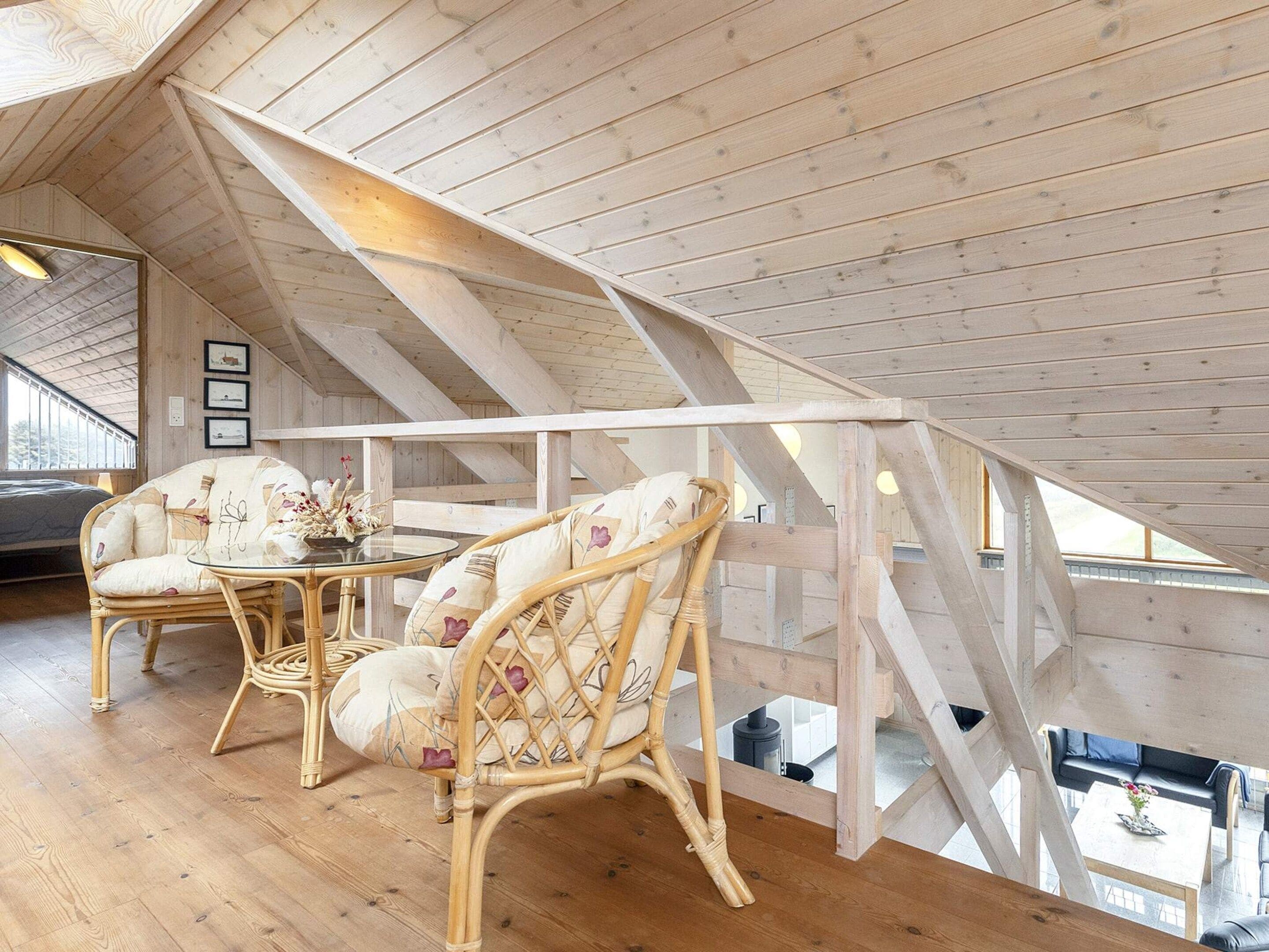 Une pièce aux hauts plafonds, avec des poutres en bois, une table en verre, des chaises en osier et une vue sur un niveau inférieur.