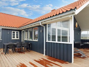 A covered outdoor area with a wooden deck, a table with chairs, and a large window.