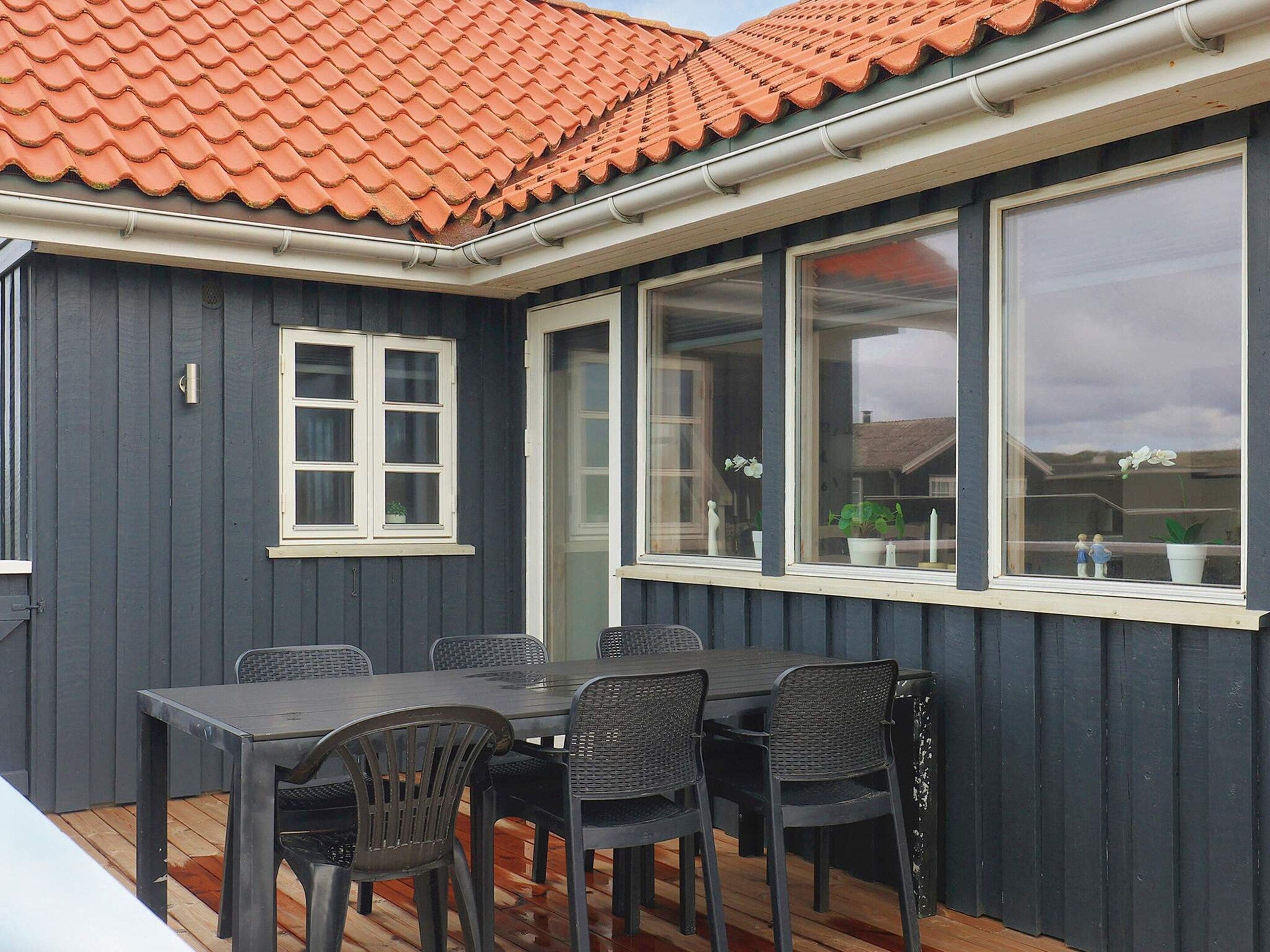 A covered patio with a table and chairs, a window with a view of the house, and a tiled roof.