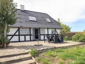 Ein traditionelles Fachwerkhäuschen mit geneigtem Dach, einer Haustür und einer kleinen Terrasse mit Sitzgelegenheiten.