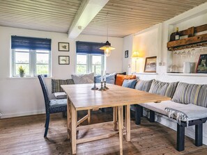 A cozy room with a wooden dining table, a sofa, a chair, and a bookshelf with glassware.