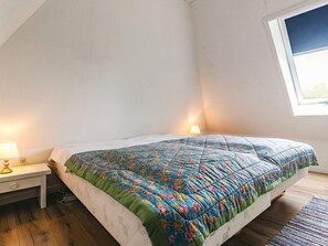 Ein Schlafzimmer mit Bett, Nachttisch, Lampe und Fenster.