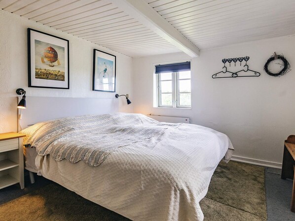 A bedroom with a bed, a desk, a chair, a window, and wall decorations including framed pictures and a wall-mounted light fixture.