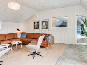 Una sala de estar moderna con un sofá modular, un sillón blanco, una mesita de centro y una lámpara de pie. Hay cuadros enmarcados en la pared y un ventanal con vistas.