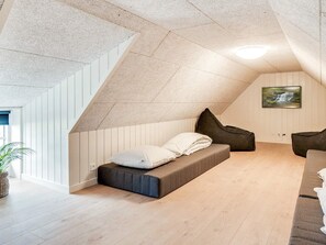 A modern loft bedroom with a sloped ceiling, a built-in bench bed, a television mounted on the wall, and a potted plant.
