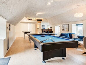 A modern living room with a pool table, a sofa, and a dining area.