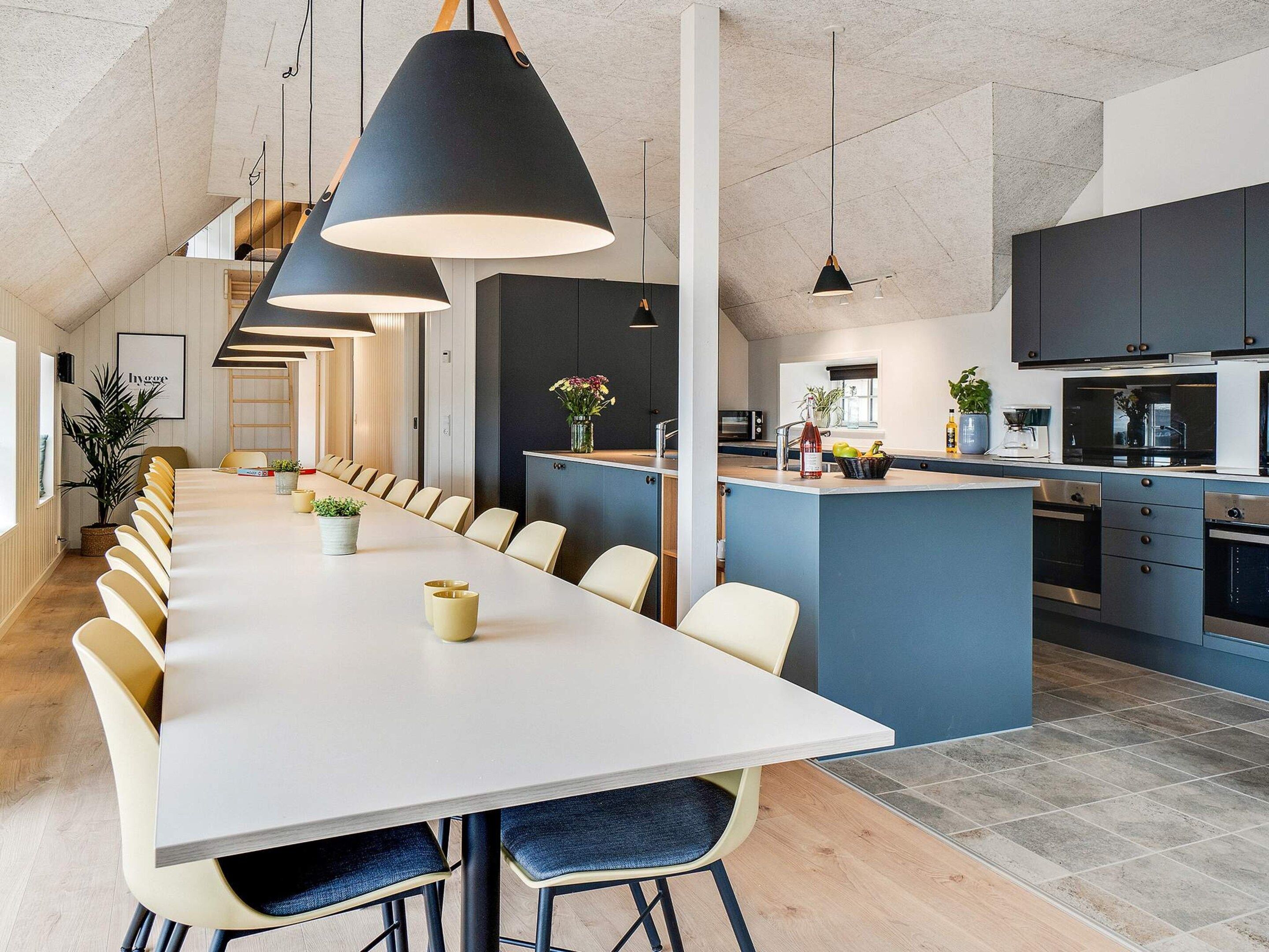 A modern kitchen with a central island, a dining area with a long table, and pendant lighting.