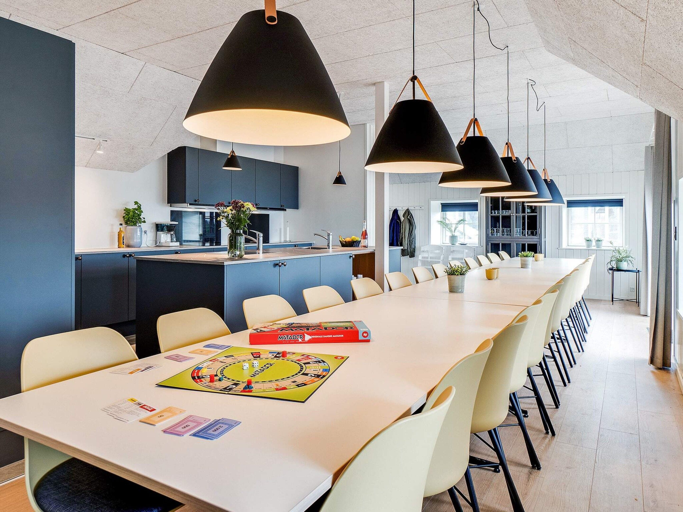 A modern kitchen with a central island, pendant lighting, and a dining area with a long table and chairs.