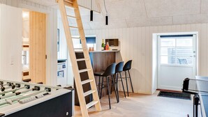 Una habitación con mesa de fútbol, zona de bar con taburetes, escalera de madera y ventana.