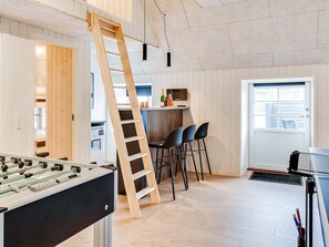 A room with a foosball table, a bar area with stools, a wooden ladder, and a window.