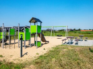 A playground with climbing structures, swings, and picnic tables. - 5 Star Holiday Home in Ringkobing (Ringkobing)