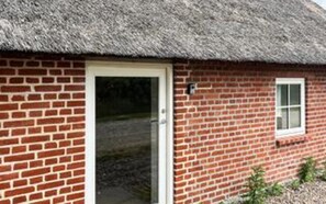 A brick building with a thatched roof, a white door, and a small window.