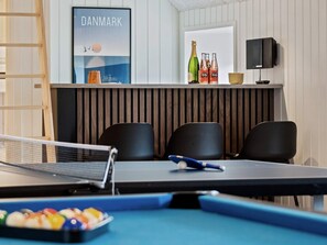 A pool table with a poster of Denmark, a bottle of champagne, and a speaker on a shelf.