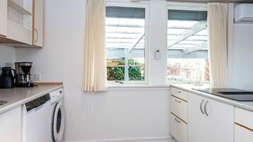 Cocina compacta con lavadora, cafetera y ventana con cortinas.