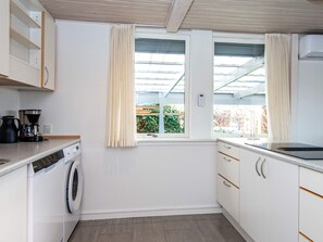 Cocina compacta con lavadora, cafetera y ventana con cortinas.