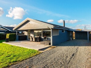 Ett modernt hus med en täckt uteplats, ett område för grillning och en grusuppfart.