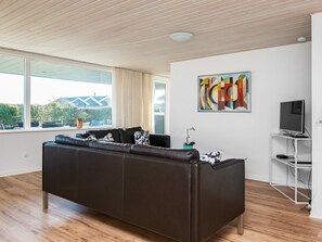 A modern living room with a leather sofa, a flat-screen TV on a stand, and a large window with curtains.